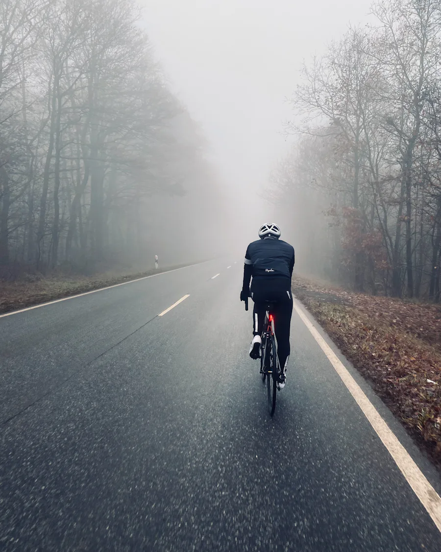 Ciclista isolado numa estrada rectilínea envolvida em nevoeiro cerrado
