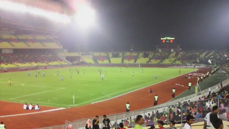Estádio com bancadas cheias durante um jogo nocturno, visto de uma das curvas