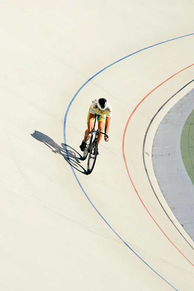 Pista de velódromo vista de cima, com linhas de marcação e um ciclista a passar na curva