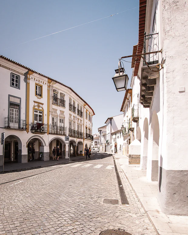 Rua estreita de calçada portuguesa entre fachadas antigas de uma vila